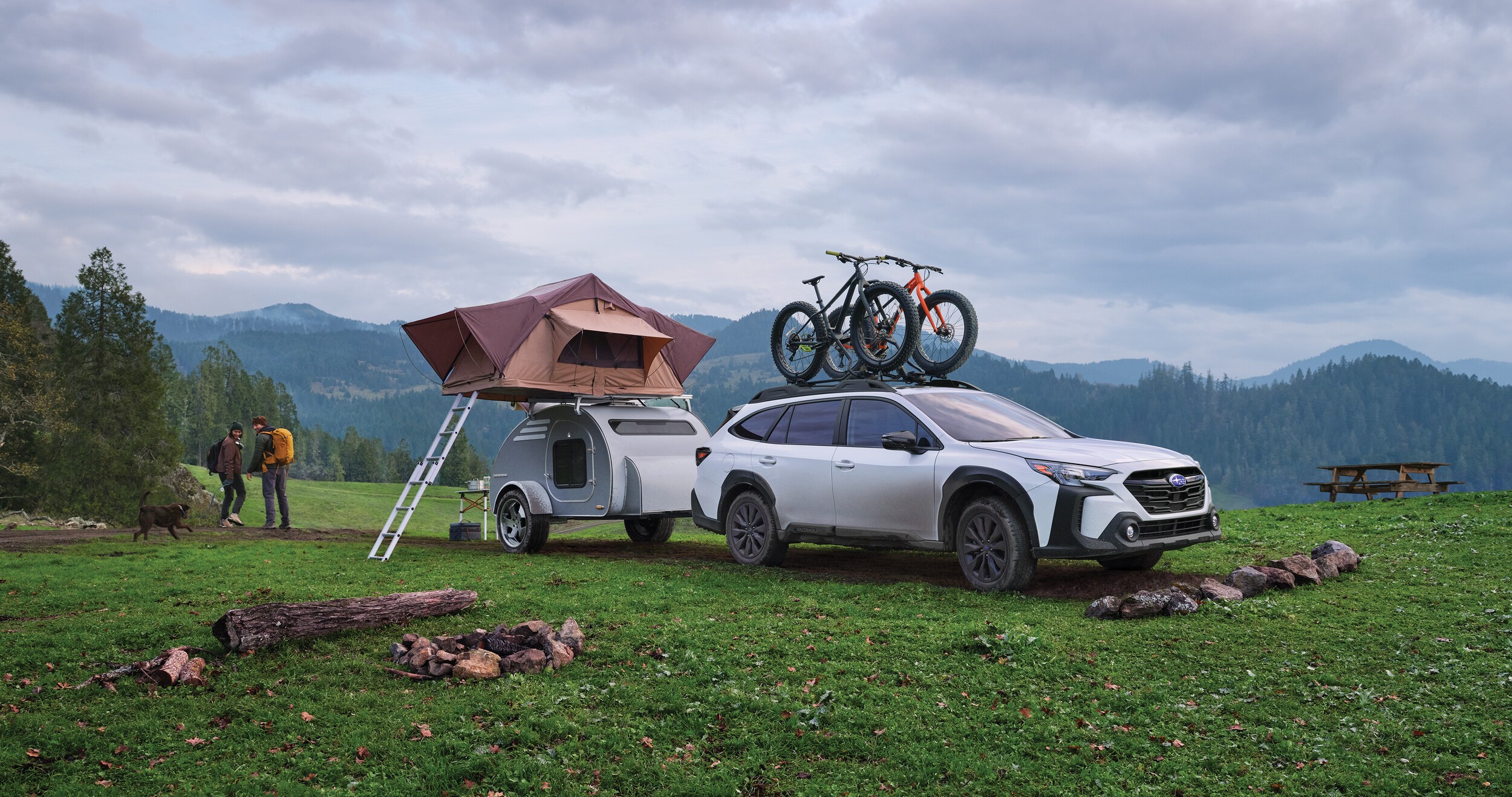 A couple getting ready for a hike near their 2023 Outback Onyx Edition, which is towing a camping trailer.