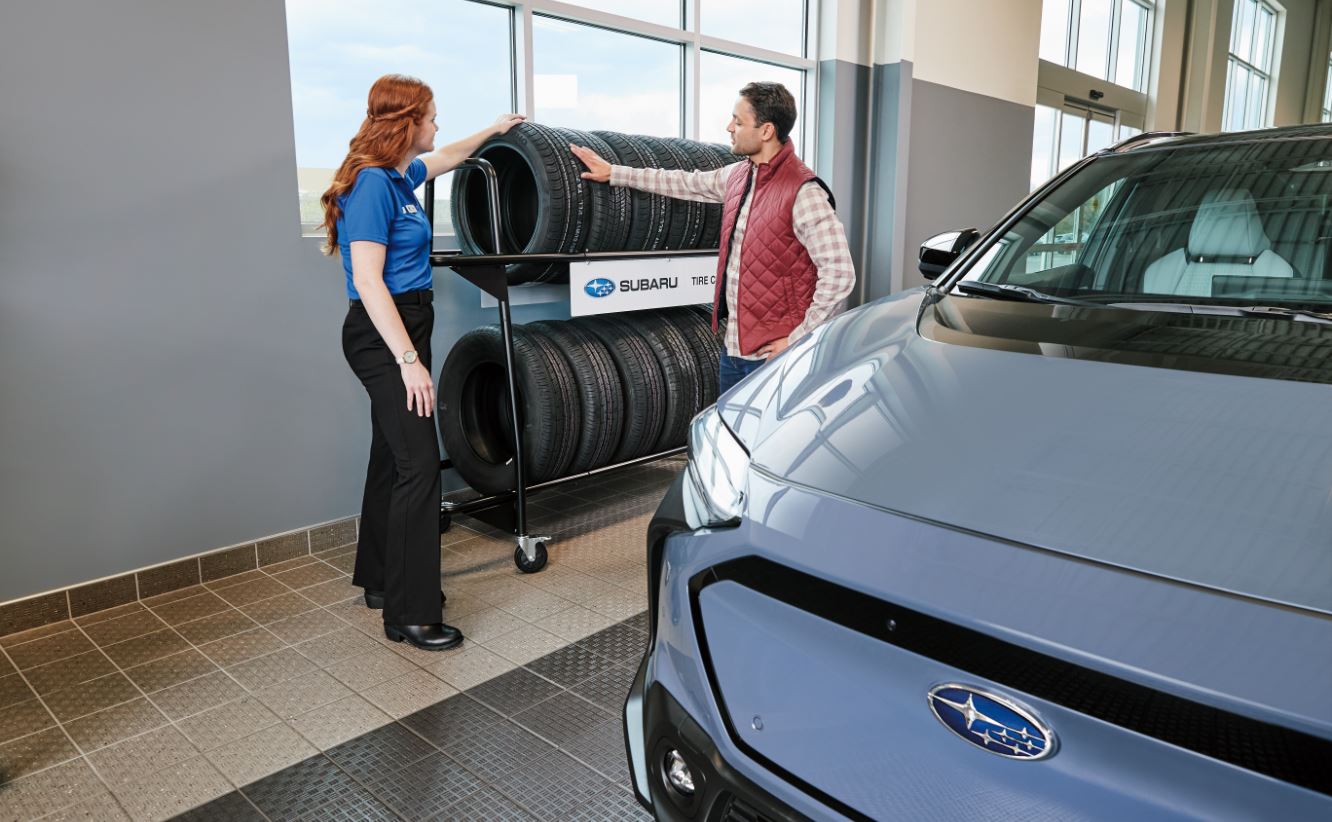 Two individuals standing next to a two-tier rack of tires located within a service drive.