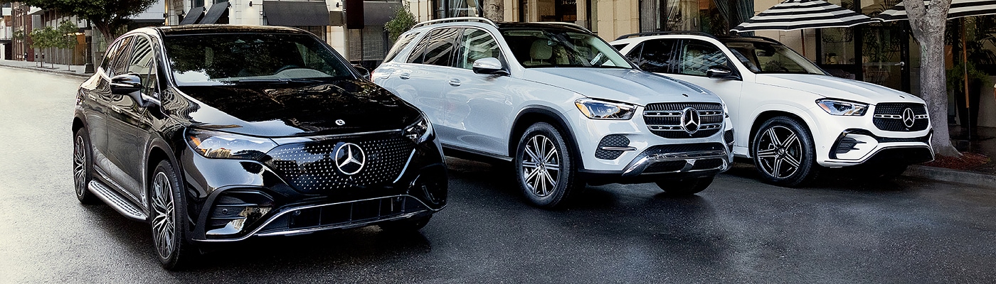 Three Mercedes-Benz SUVs parked on a city street near a cafe