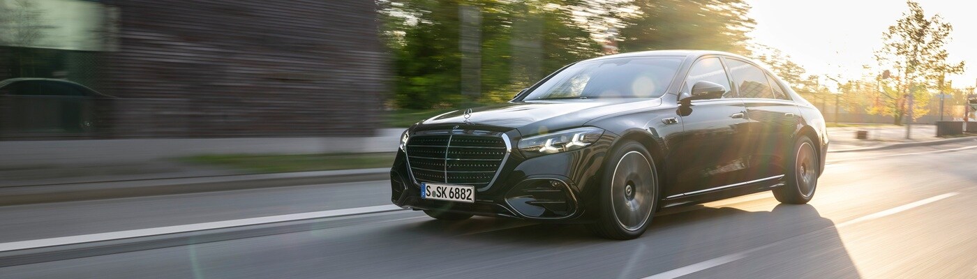 Black Mercedes-Benz S-Class driving on a road at sunset