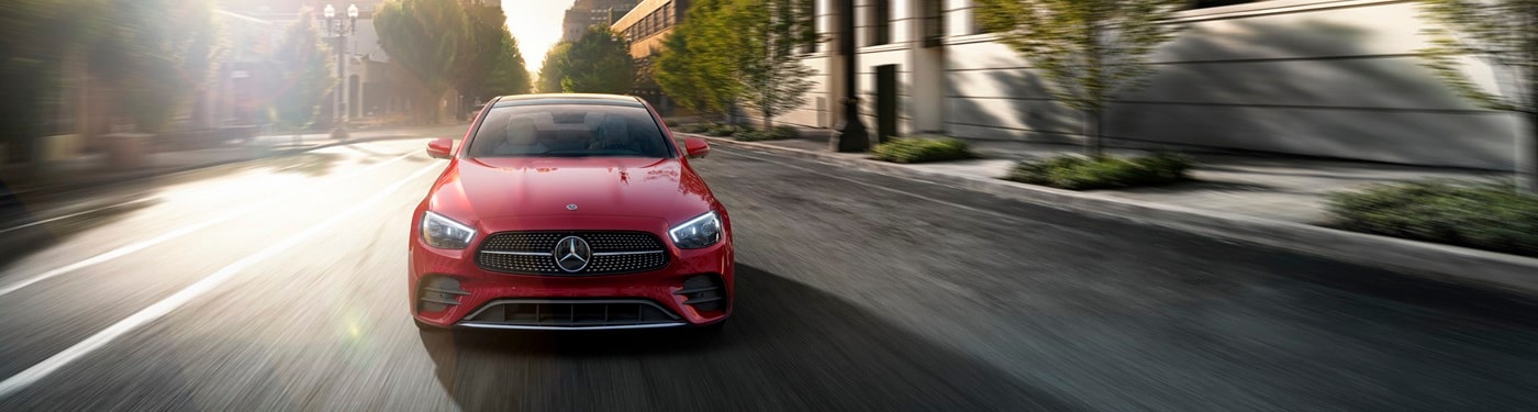 Red Mercedes-Benz E-Class Sedan driving head on a city street