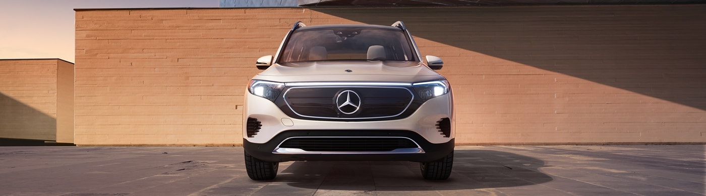 White Mercedes-Benz EQB parked near a stone wall in amber light