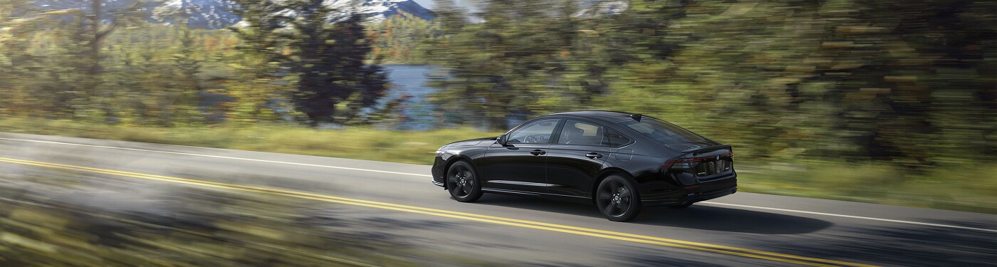 Black Honda Accord Hybrid Sport L driving on a road in the forest