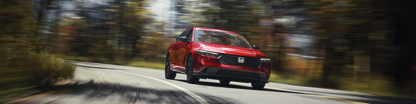 Red Honda Accord Hybrid Sport L driving on a road in the forest