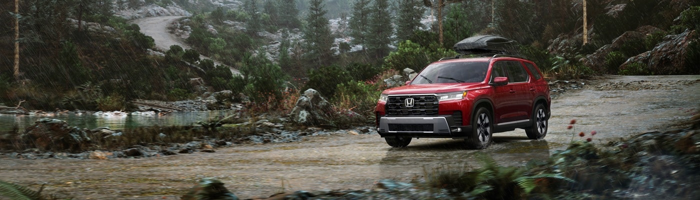 Red Honda Pilot Elite driving on a rainy road in the woods