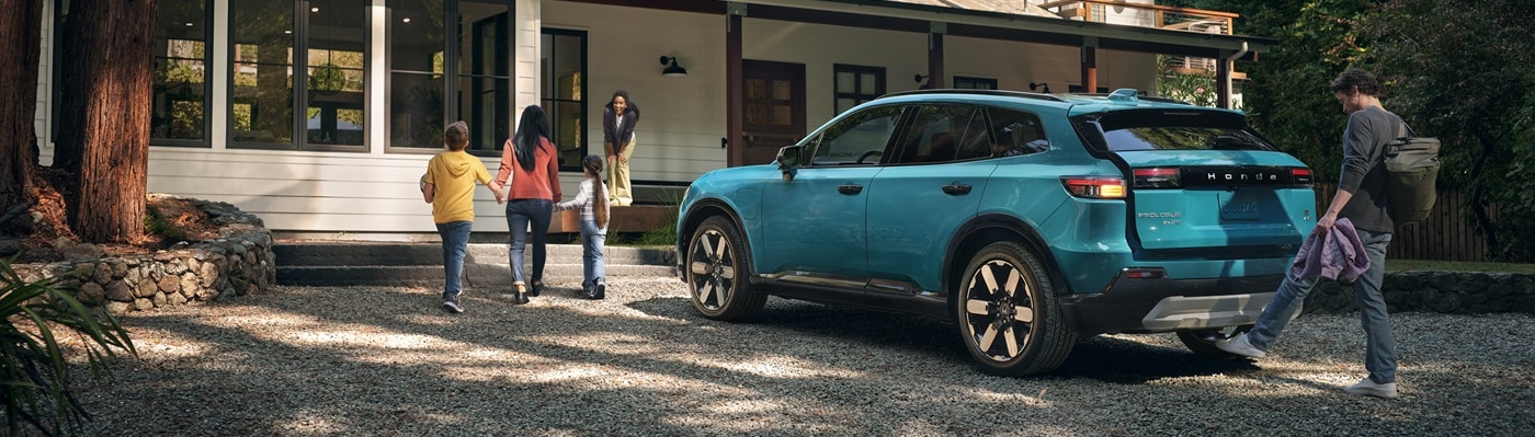 Blue Honda Prologue Elite parked in front of a home in the woods