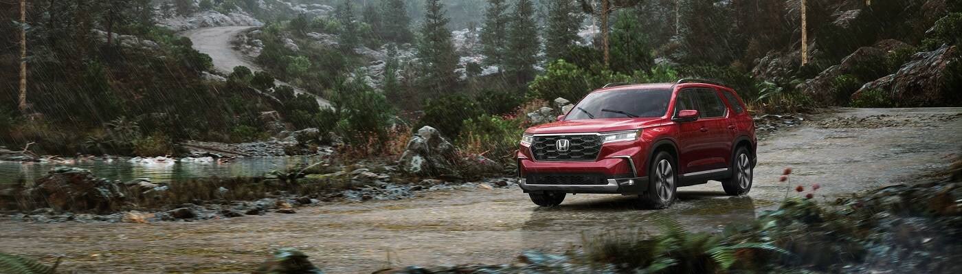Red Honda Pilot Sport driving on a dirt road in the forest