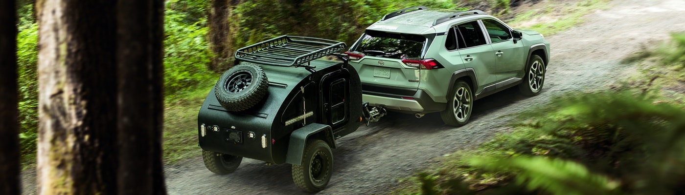Green Toyota RAV4 Adventure towing a camper in the woods