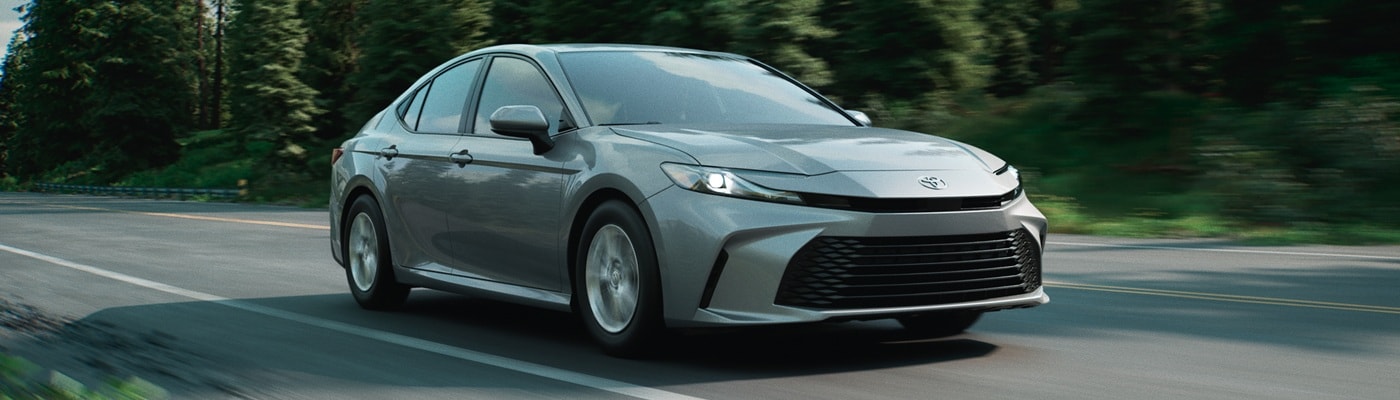 Grey Toyota Camry LE driving on a road in the forest