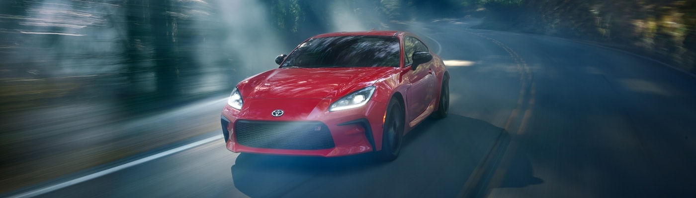 Red Toyota GR86 driving on a road in the forest