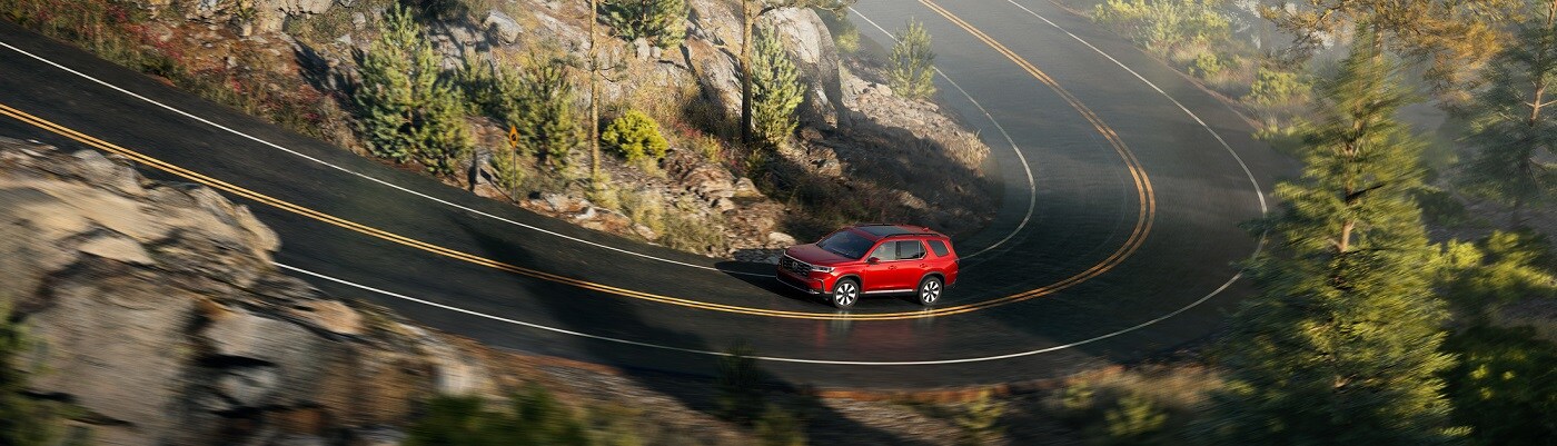 Honda Pilot Elite Red Honda Pilot Elite driving on a winding road in the forest