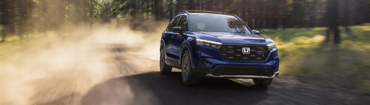 Blue Honda CR-V Hybrid TrailSport driving on a dirt road in the forest