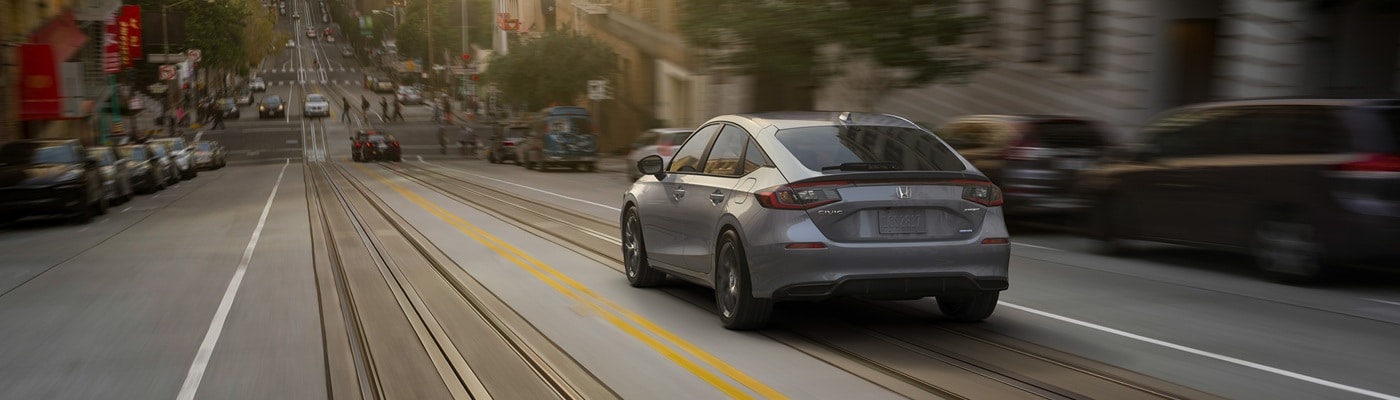 Honda Civic Hatchback Grey Civic Hatchback Sport Touring Hybrid driving down a hill in the city