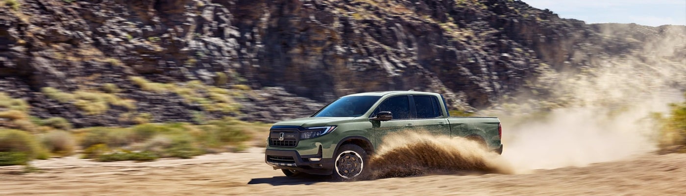 Green Honda Ridgeline truck driving thru sand