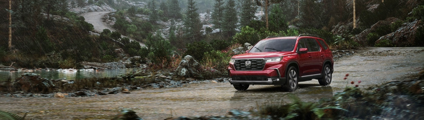 Red Honda Pilot Elite driving in a rainy forest