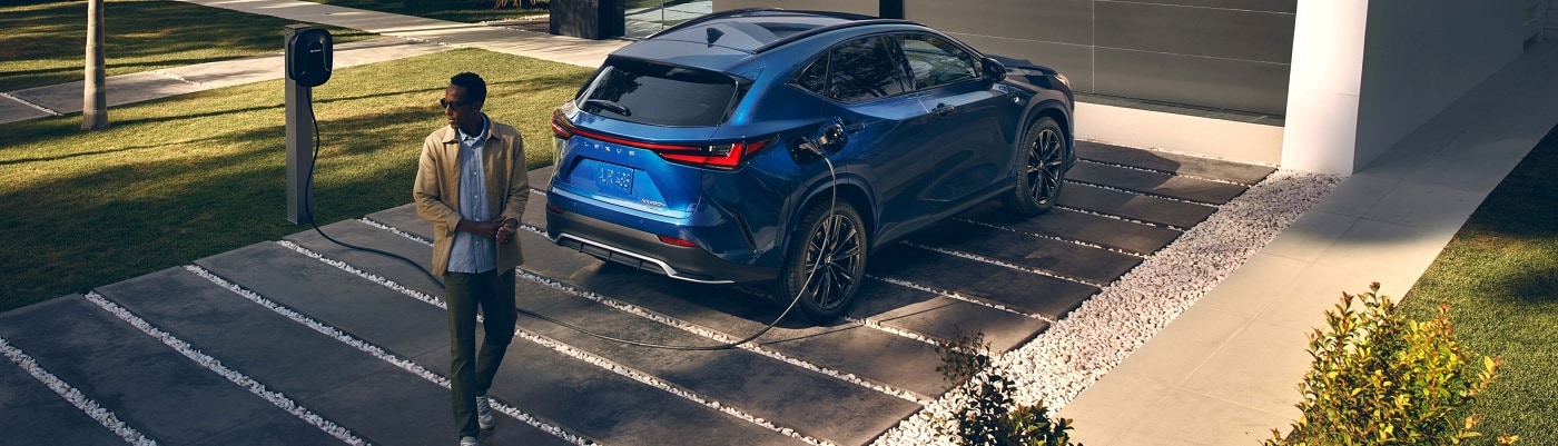Blue Lexus NX charging by a modern house
