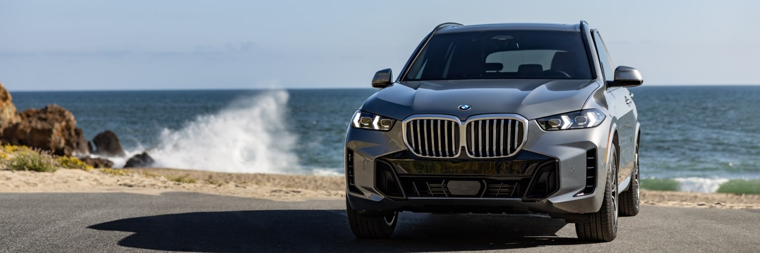 BMW X5 PHEV SUV parked front facing with the ocean in the background
