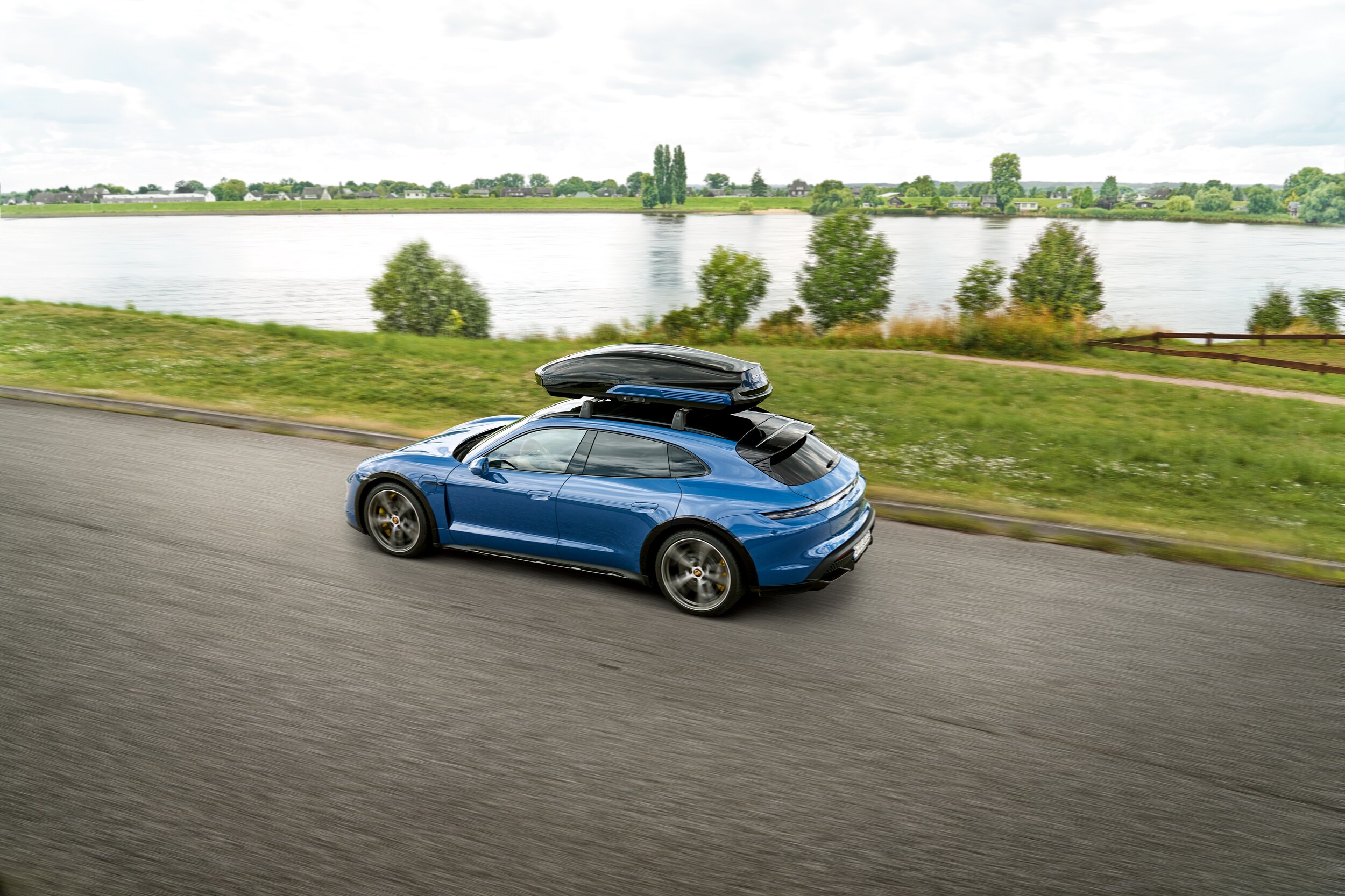 Porsche Taycan Turbo S Cross Turismo Blue Taycan Cross Turbo S Turismo driving on a road by a lake