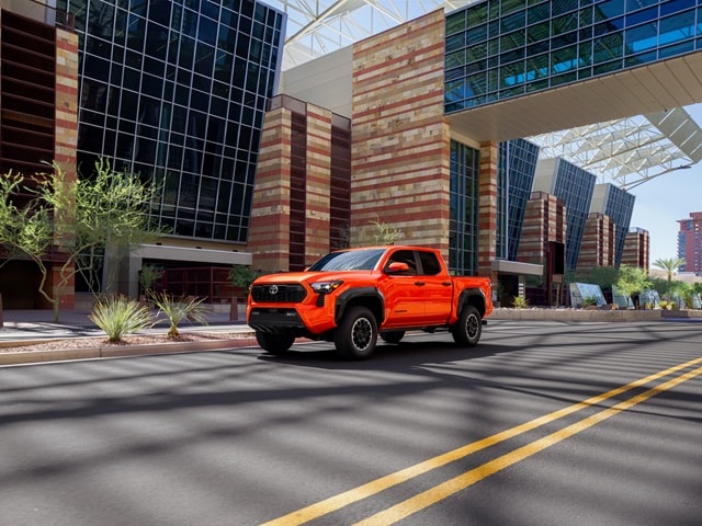 Orange Toyota Tacoma driving on a city road in the desert