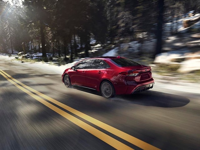 Red Toyota Corolla Hybrid driving on a snowy forest road