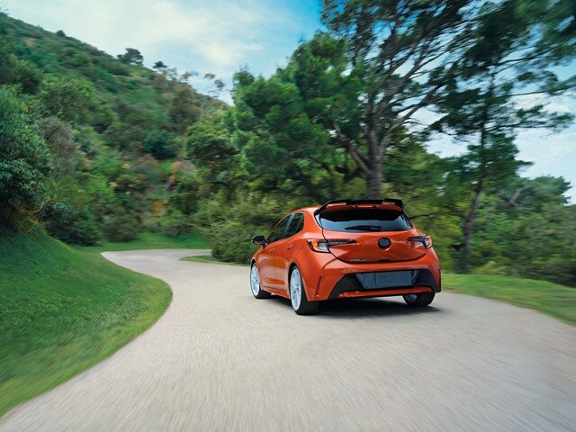 Orange Toyota Corolla Hatchback FX driving away on a rural road