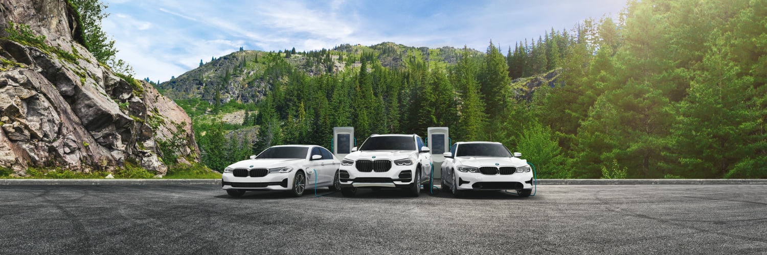 three white BMW plug-in electric vehicles charging in a scenic mountain spot