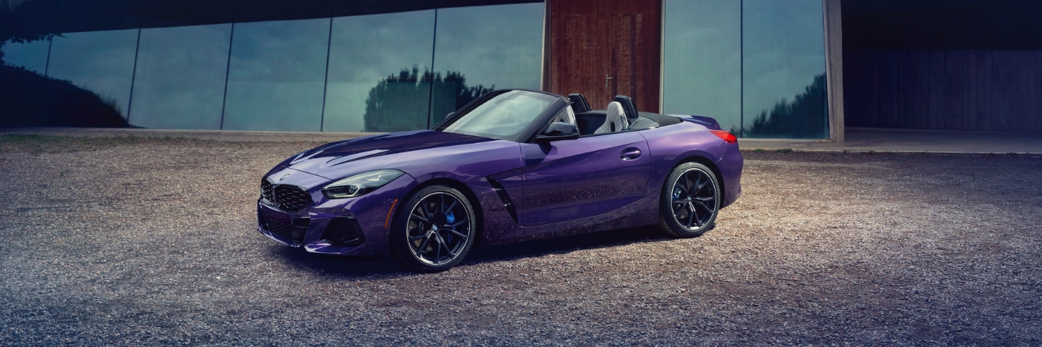 purple BMW Z4 convertible parked on gravel in front of a building