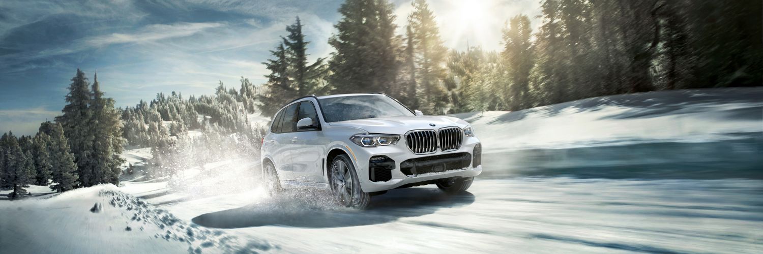 white BMW X5 driving up a mountain on a snow-covered road