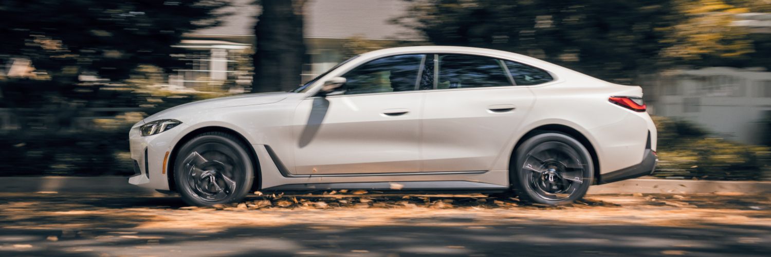 BMW i4 side view of a white BMW i4 sedan driving down a residential street in autumn