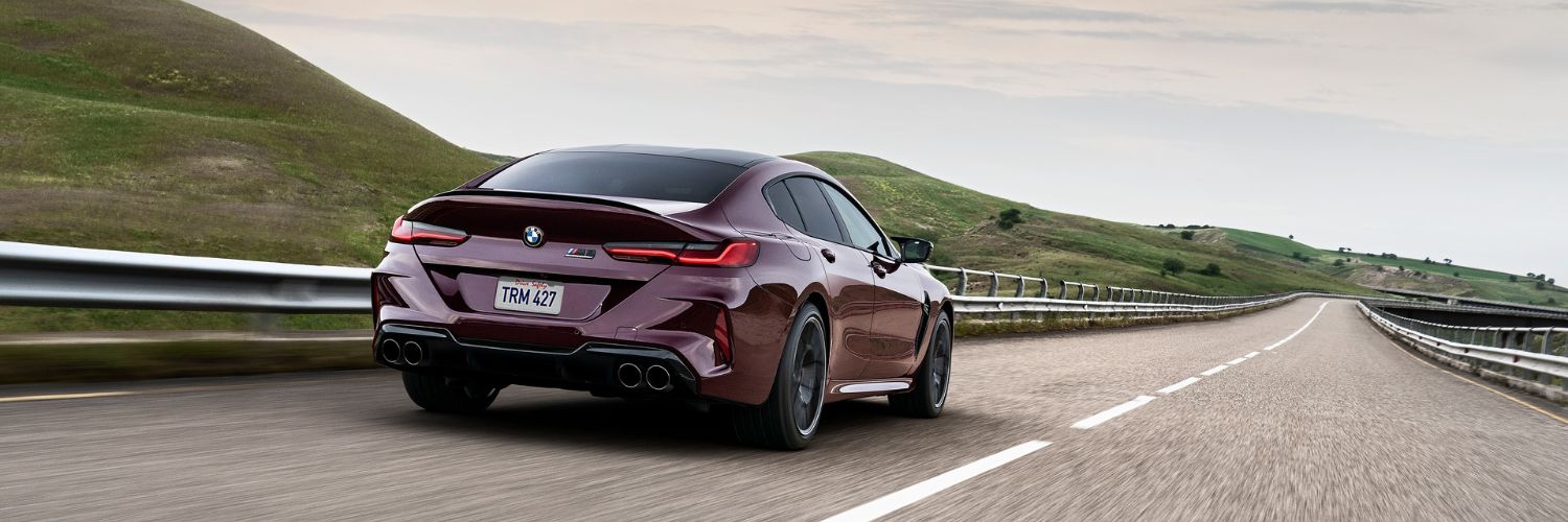 BMW M8 BMW M8 Gran Coupe driving away from the camera on a road through the countryside