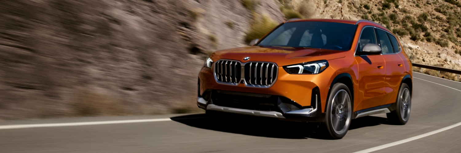 orange BMW X1 SUV driving up a curvy mountain road
