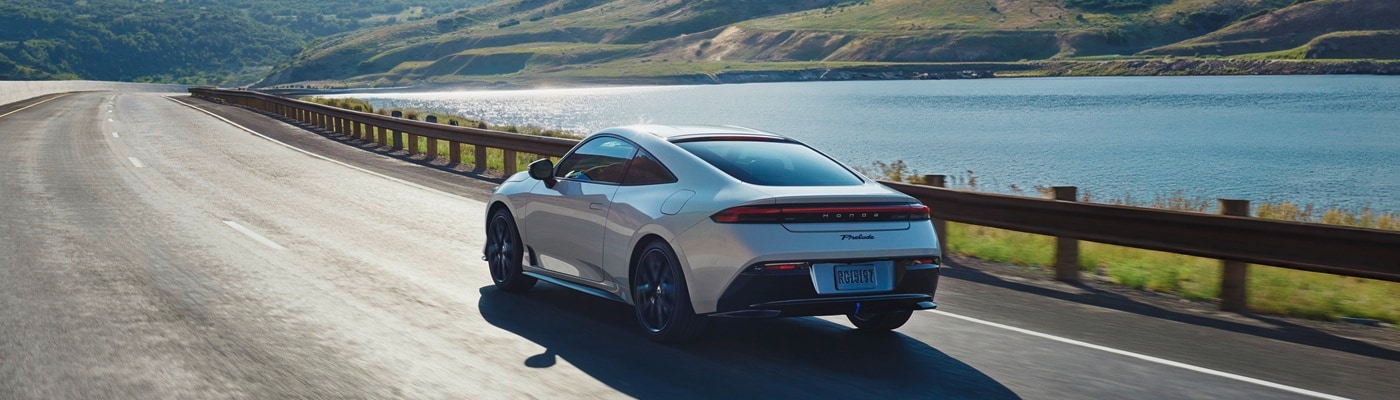 White Honda Prelude driving on a road near a reservoir