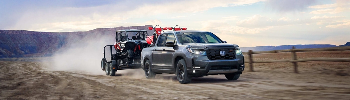 Grey Honda Ridgeline TrailSport towing a trailer across the desert