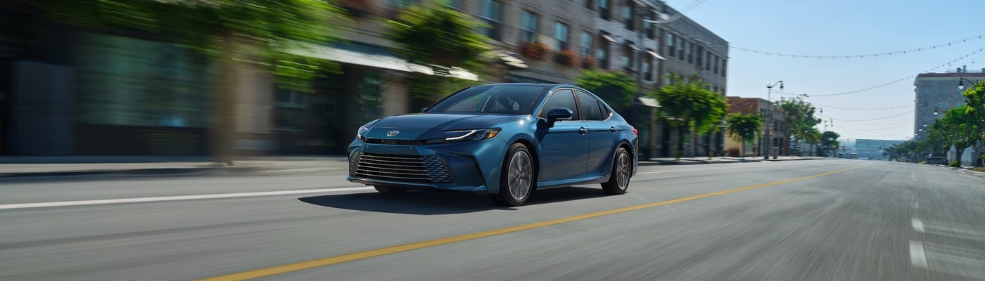 Blue Toyota Camry XLE driving on a road in a city