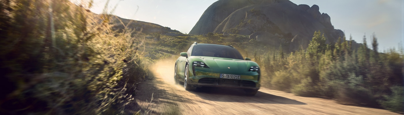 Green Taycan Cross Turismo driving on a dirt road in the desert