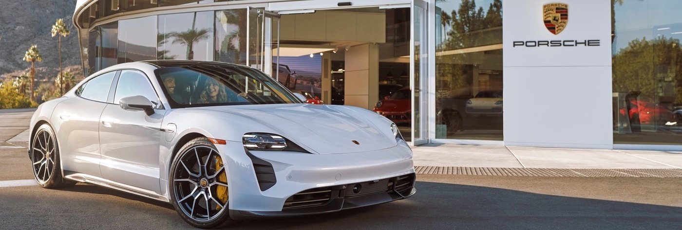 White Porsche Taycan parked in front of a Porsche Center