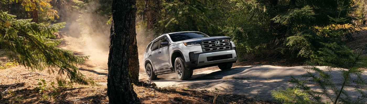 White Honda Pilot TrailSport driving on a dusty road in the forest