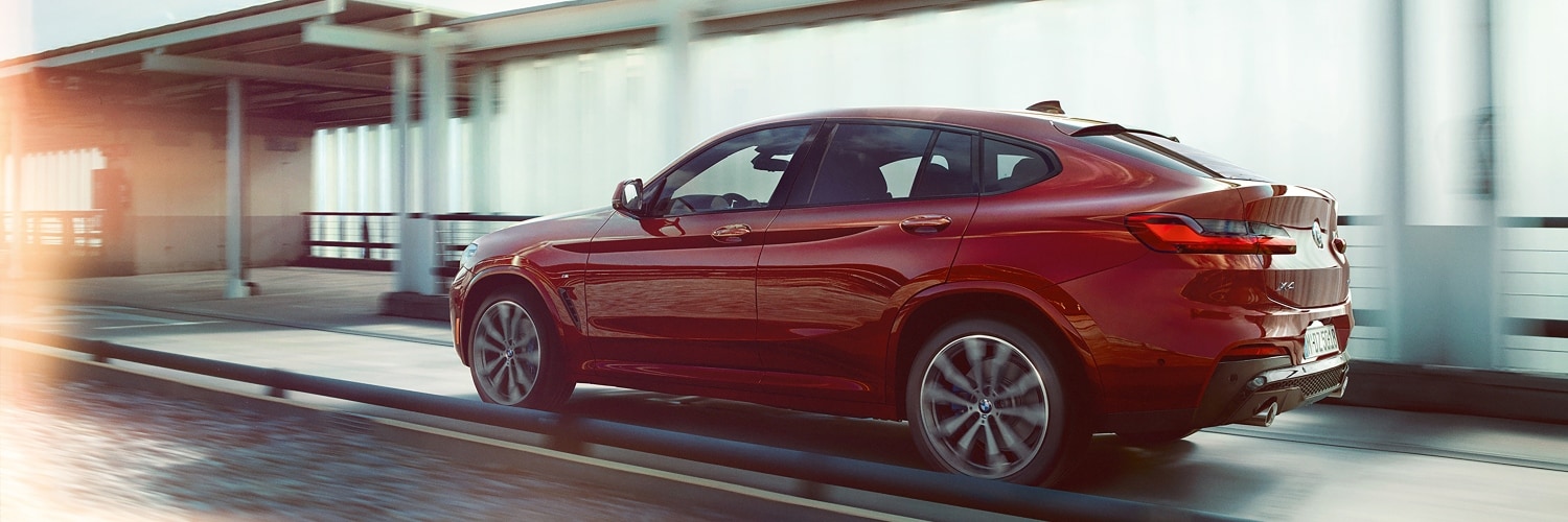 BMW X4 side view of a red BMW X4 driving on a mountain road with a blurred background