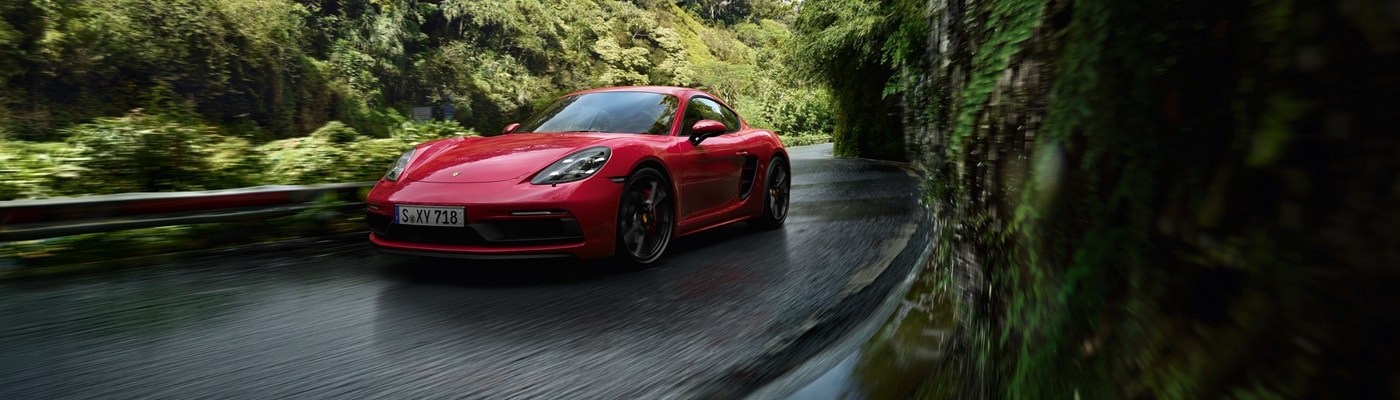 Red Porsche 718 Cayman GTS driving on a road in the jungle