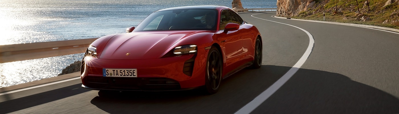 Red Porsche Taycan driving on a winding road on the coast