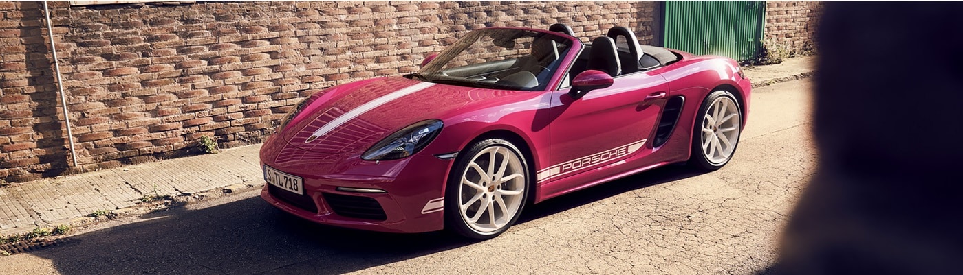 Pink Porsche 718 Boxster Style Edition convertible parked by a brick wall