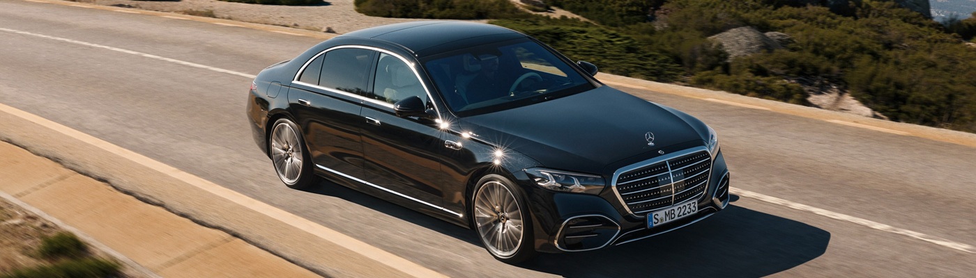 Black Mercedes-Benz S-Class driving on a sunny and hilly road