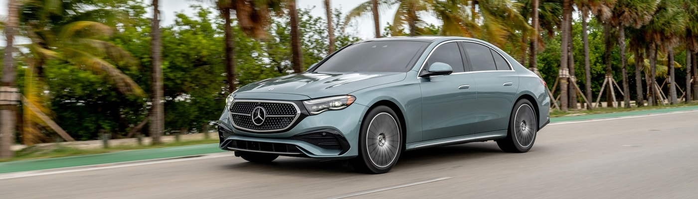 Mercedes-Benz E-Class Sedan driving on a city street with palm trees