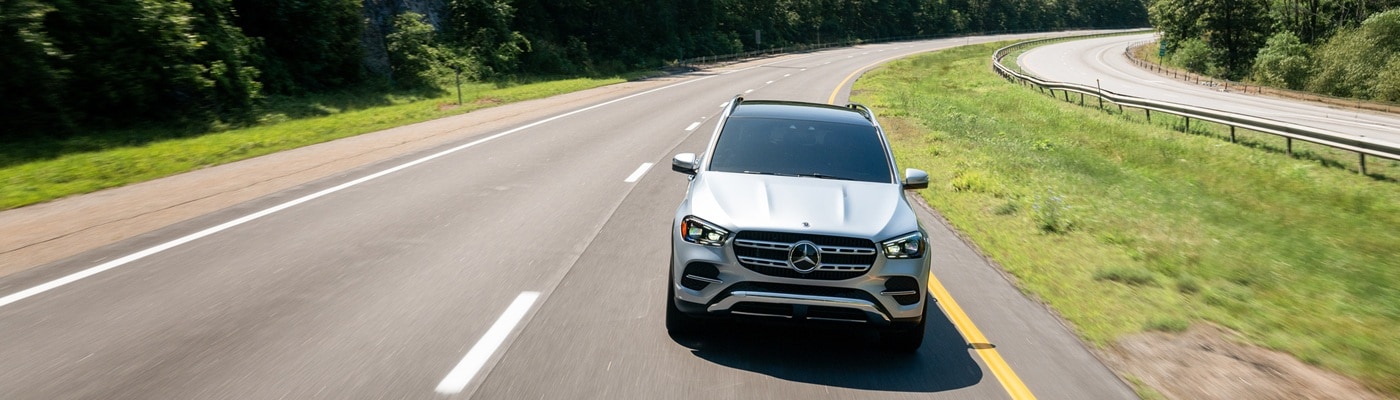 Silver Mercedes-Benz GLE 450 driving on a highway in the forest