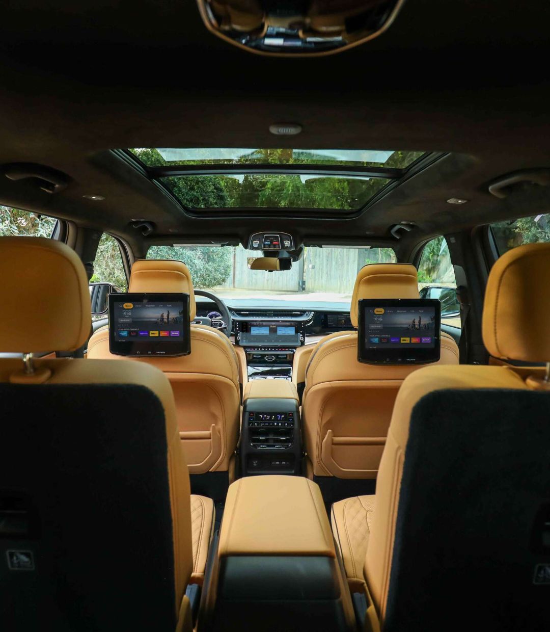 Spacious Jeep three-row interior with tan seating, dual rear entertainment screens, and a panoramic sunroof.