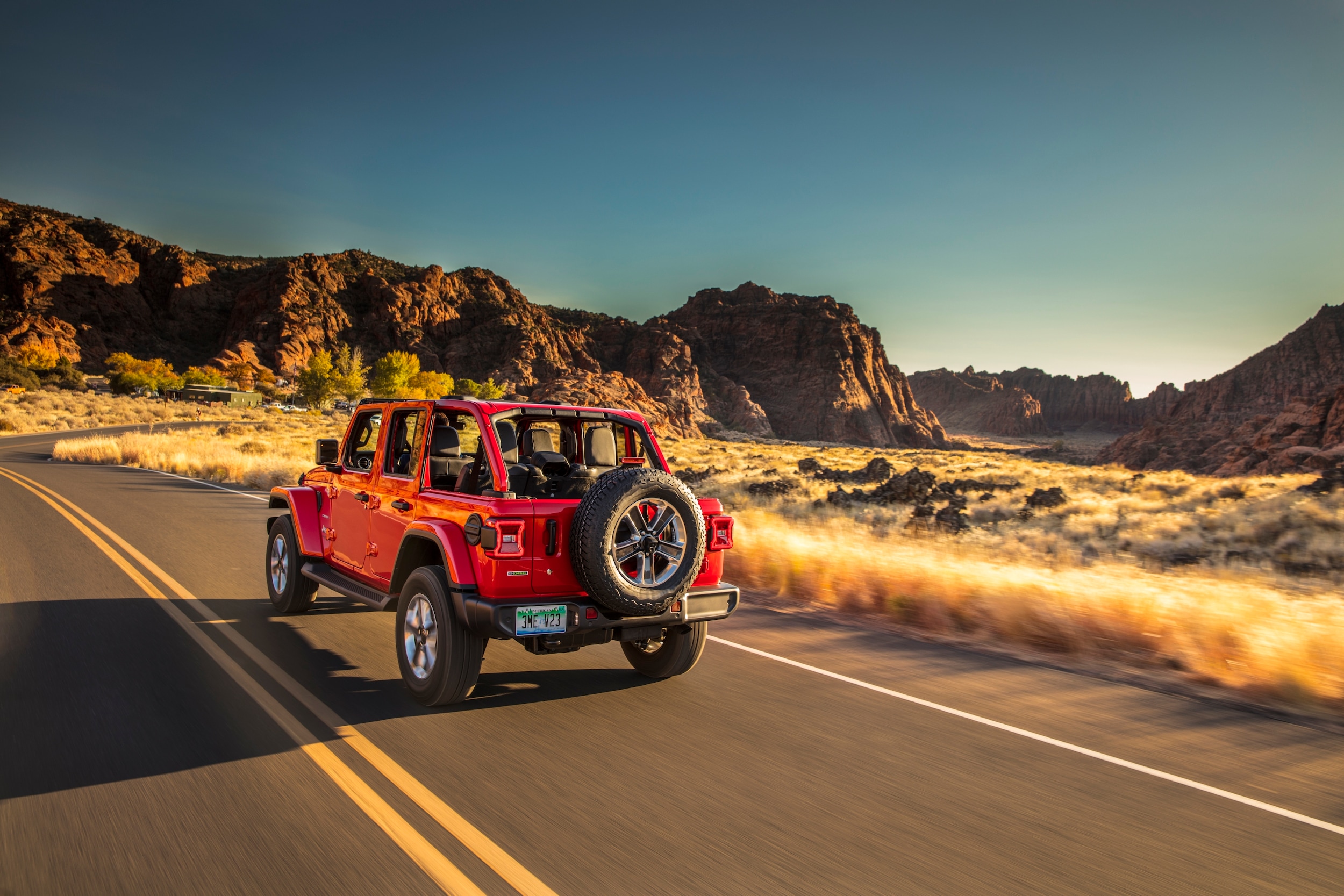 Red Jeep Wrangler Driving on Road surrounded by field and canyons at Sunset