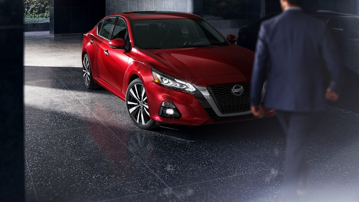 Guy walking around red Nissan Altima front 3/4 view