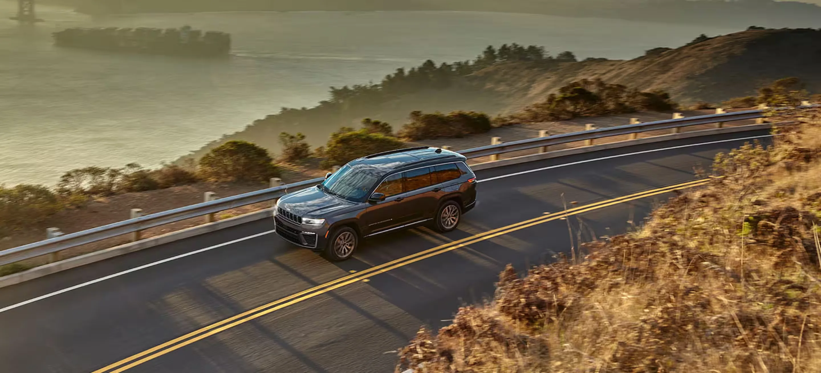 A gray Jeep Grand Cherokee L Summit on a coastal road, the long-wheelbase three-row version