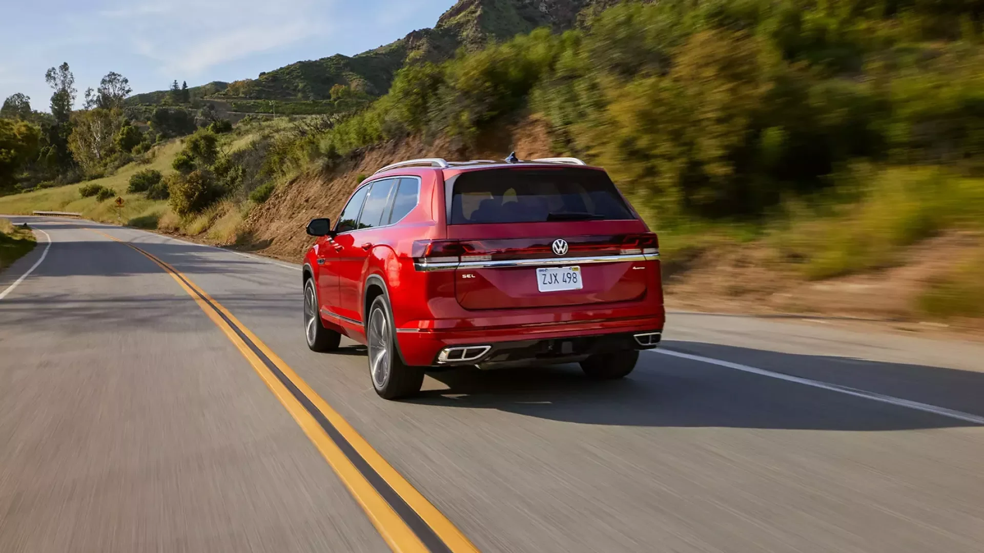 2026 Volkswagen Atlas in aurora red metallic driving on a wooded road