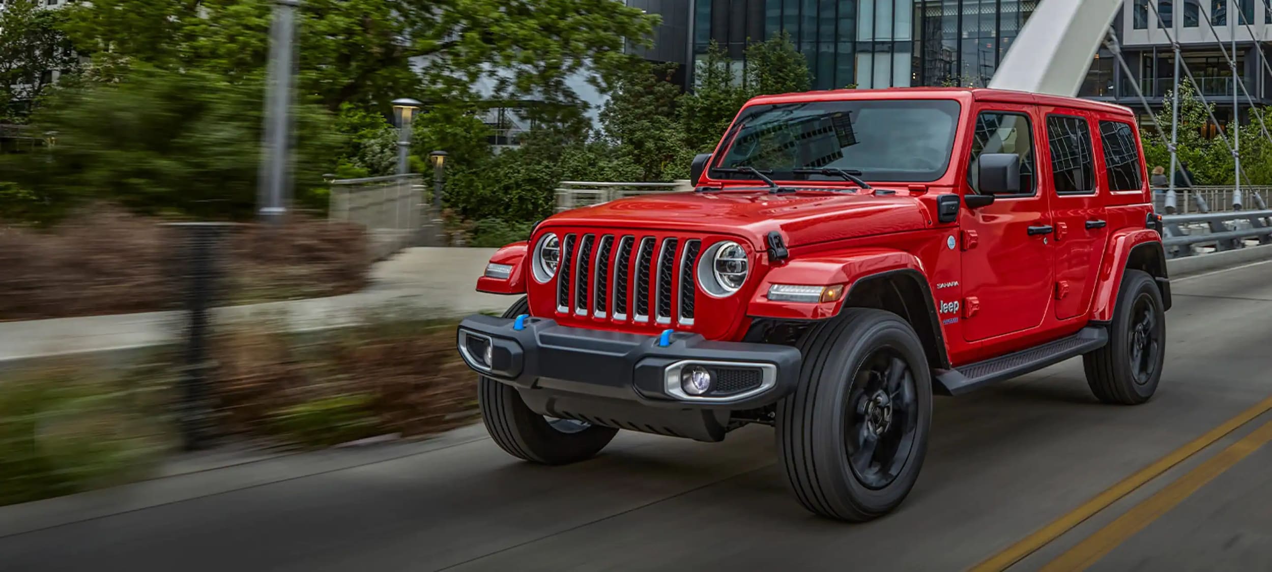 Red Jeep Wrangler 4xe driving over a bridge through the city